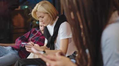 Üniversite kütüphanesinde telefonlarının başında kameraya yakın duran iyi görünümlü bir öğrenci grubu.