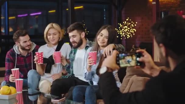 Duas senhoras bonitas e dois cara atraente s enquanto sentado no sofá tirar fotos para memórias que se sentem felizes e sorrindo grande — Vídeo de Stock