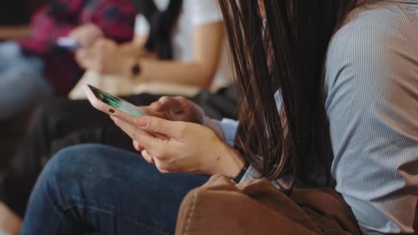 Detalhes de close-up jovens estudantes em uma biblioteca universitária gastando tempo em seus telefones, enquanto têm uma classe livre — Vídeo de Stock