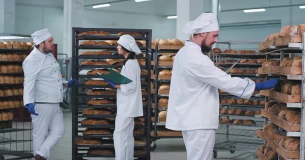 Bien parecido tres panaderos en una panadería después de cargar el pan en los estantes chef principal tomando fotos de pan recién horneado. mociones lentas — Vídeos de Stock