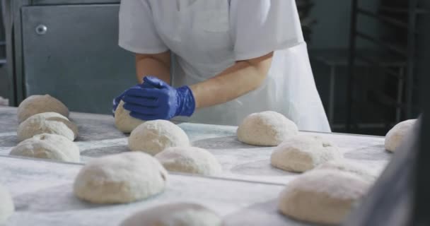 Pékeket dolgoznak egy nagy pékségben, előkészítik a tésztát, hogy a sütőgépben süssenek. lassú mozdulatok — Stock videók