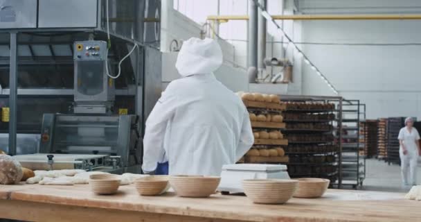 Перемещение харизматичный пекарь с беспроводными наушниками танцует во время работы за столом с тестом в большой хлебопекарной промышленности. медленный — стоковое видео