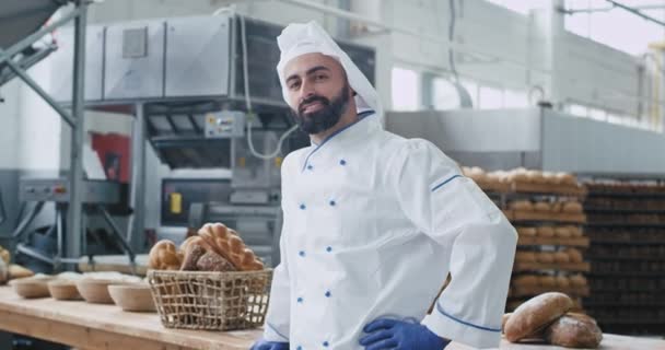 Buen ambiente en la industria de panadería grande sonriendo gran chef panadero mirando directamente del retrato de la cámara, canasta vintage de fondo con pan orgánico . — Vídeo de stock