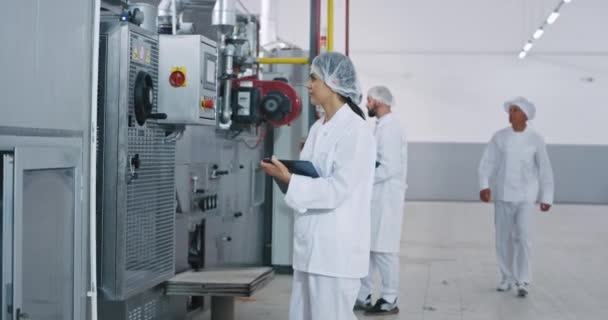 Хлібопекарська промисловість двоє молодих інженерів з електронним планшетом перевіряють сучасну промислову машину старого хлібобулочного чоловіка, який ходить навколо, вони всі носять спеціальну уніформу — стокове відео