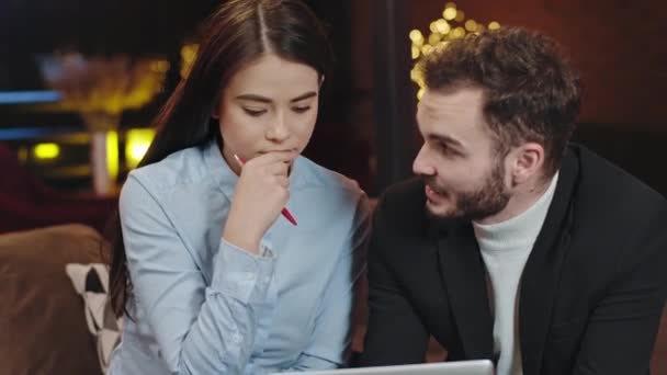 Good looking guy office manager and his assistance attractive lady analyzing a plan of work and statistic while sitting on the sofa closeup to the camera — ストック動画