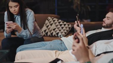 Üniversite kütüphanesinde akıllı telefonlarıyla oturan genç öğrenciler öğle yemeği yerken sosyalleşiyorlar ve rahatlıyorlar.