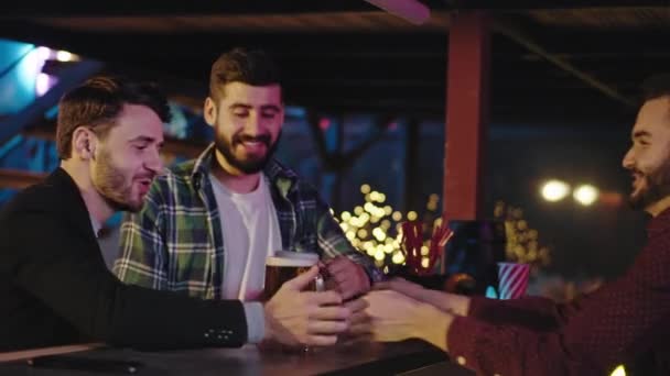 Gut aussehende Freunde, die eine gute Zeit in einer Kneipe verbringen, trinken sie ein kühles Bier aus einem großen Glas und genießen den Abend — Stockvideo
