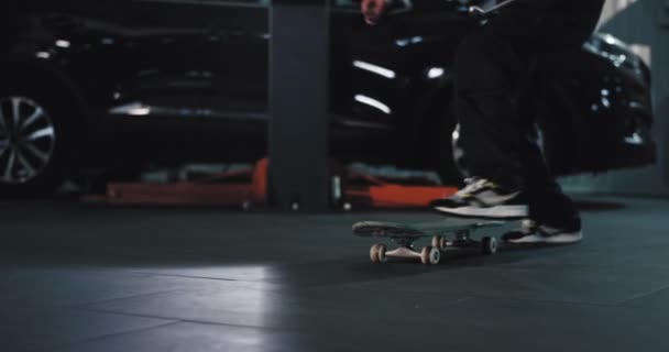 Молодий механік в гаражі розважається він бере скейтборд і насолоджується часом на роботі — стокове відео
