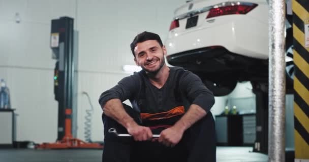 Portrait in a garage mechanic guy in a uniform smiling large and looking straight to the camera before starting his work — Stock Video