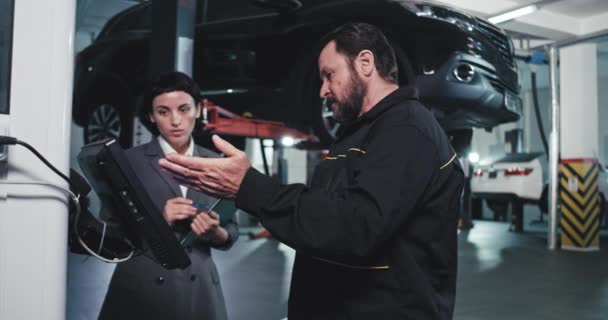 In front of the camera in the modern auto center main mechanic and manager lady using the services computer analyzing the plan of work — 비디오