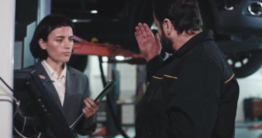 Oto hizmet merkezindeki iyi görünümlü ciddi kadın yönetici, ana müdürle iş planını incelerken ve bilgisayar kullanırken sohbet ediyor.