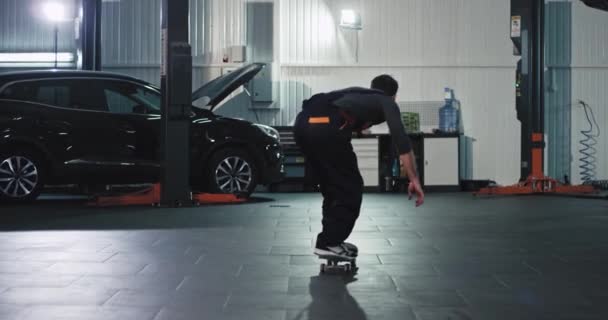 Em grande auto serviço centro mecânico cara em um uniforme tomar um skate e ter um grande momento em seu local de trabalho — Vídeo de Stock