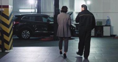 Modern bir otomobil hizmet merkezinde ofis yöneticisi kadın ve yetişkin bir tamirci kameranın önünde bir şeyi analiz ediyor.
