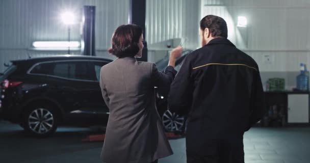 Επιχειρηματίας γυναίκα σε ένα κοστούμι και ο κύριος μηχανικός από το γκαράζ έχουν μια φιλική συνομιλία στο κέντρο εξυπηρέτησης αυτοκινήτων χαμογελούν και αισθάνονται μεγάλη — Αρχείο Βίντεο