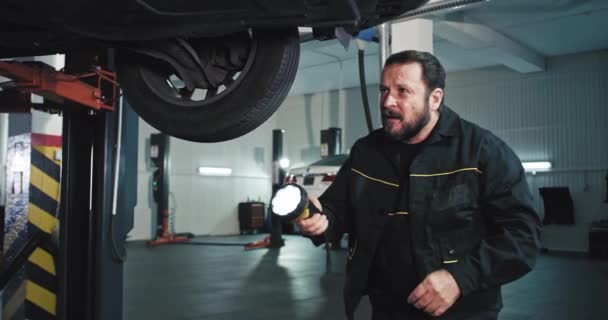 Gut aussehende Mechaniker Mann mit einer Taschenlampe kam er zum Auto und beginnen zu arbeiten versuchen, das Problem der beschädigten Auto zu finden — Stockvideo