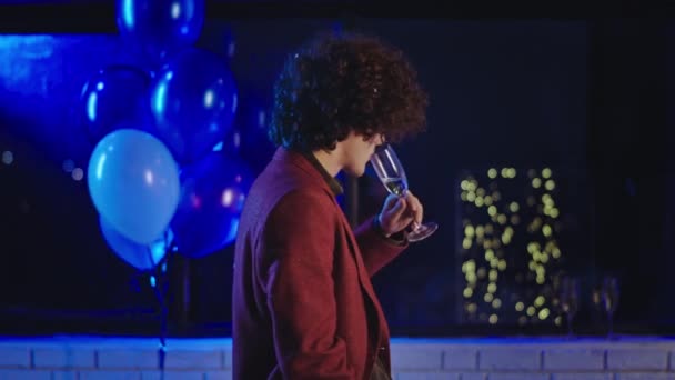 Estudante festa carismático cara com cabelo encaracolado beber um pouco de vinho espumante e desfrutar da noite na festa — Vídeo de Stock