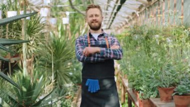 Çekici bahçıvan kendi çiçek serasında büyük bir gülümsemeyle kameraya bakıyor ve büyük bir gülümseme sergiliyor.