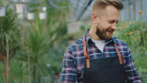 Le stor trädgårdsmästare närbild till kameran ta en dekorativ blomma i potten och titta rakt mot kameran har han en mycket upphetsad ansikte — Stockvideo