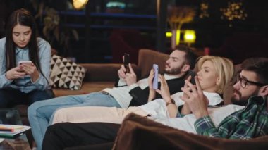 Molada konsantre olmuş çekici öğrenciler vaktlerini akıllı telefonlarıyla kütüphanede kanepede otururken bir şeyleri analiz ederek geçiriyorlar.