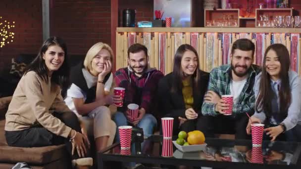 Carismático grupo multiétnico de estudiantes que se reúnen en la biblioteca de la universidad y ven un programa de comedia sonriendo a lo grande mientras están sentados en un sofá grande — Vídeos de Stock