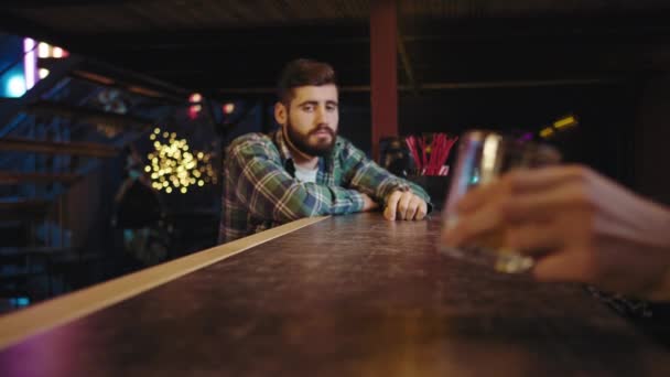 Egy bárban egy fiatal srác várja az italát a bárpultnál, a csapos odaadja a poharat a vendégnek, és örül, hogy inni kezd. — Stock videók