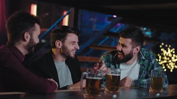 Chicos atractivos buenos y viejos amigos que se reúnen en un pub bebiendo cerveza de grandes vasos y vítores que sonríen grandes y se sienten muy bien. 4k — Vídeo de stock