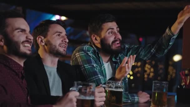 I en pub dricker goda vänner öl från ett ölglas och tittar på koncentrerad favorit match på tv de skriker och är mycket glada medan du tittar på en TV-spel — Stockvideo