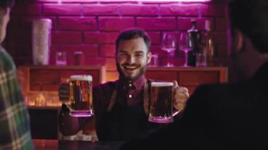 Modern bir barda mutlu ve yakışıklı bir barmen bar masasındaki büyük bardaklara bira veriyor.