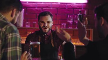 Harika bir bar. Büyük barmen müşteriye iki bardak bira veriyor. Mutlu ve heyecanlı bir şekilde içiyorlar.