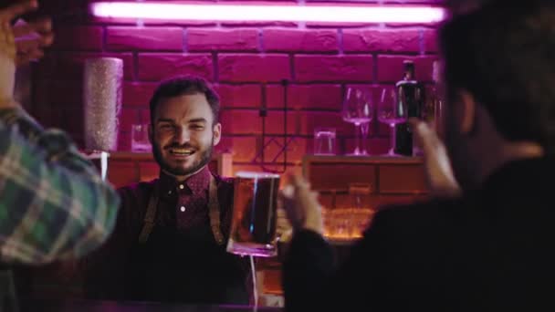 Groupe d'amis dans un pub heureux et excité attendant une sorcière de pub de bière souriant grand barman leur donnant ils acclament avec des verres et commencent à boire. Tourné sur ARRI Cinema Camera — Video