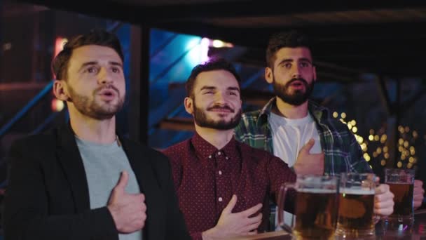 Carismáticos tres tíos en un pub frente a la cámara cantando el himno de su equipo favorito antes de empezar el partido — Vídeo de stock