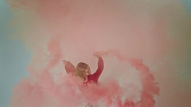 Güzel bir bayan dansçı stüdyonun içinde elinde renkli bir sis bombası tutarak video çekerken iyi vakit geçirir ve eğlenir.