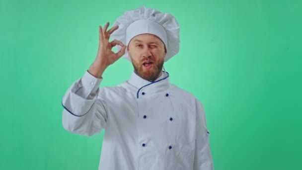Великолепный на вид пекарь, очень харизматичный внутри зеленой студии, позирующий перед камерой, он жестикулирует из рук, показывая добрый и улыбчивый — стоковое видео