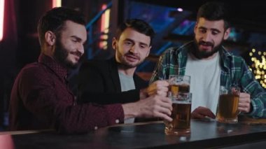 Karizmatik, yakışıklı, gülümseyen iri adamlar barda büyük bardakta birayla şerefe içerler. Bar masasında içerken birlikte eğlenirler.