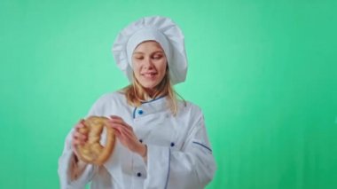 Chroma Key stüdyosundaki çekici fırıncı kadın kameranın önünde aynı anda hem taze kraker yiyip hem de dans ediyor.