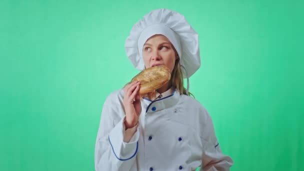 Goed uitziende bakker vrouw eten met lust zeer aantrekkelijk een frisse Franse pretzel ze op zoek naar de camera maken een voorwoord in een chroma key studio. Neergeschoten op Arri Alexa Mini — Stockvideo