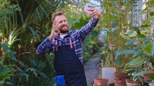 Hombre jardinero grande feliz y sonriente tomar selfie con su teléfono inteligente en un gran invernadero — Vídeos de Stock