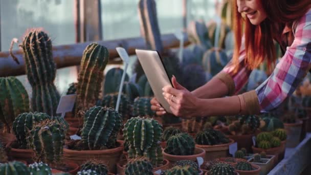 Close-up van de camera rode dame met behulp van tablet neem een aantal foto 's van de decoratieve planten in een grote industriële kas — Stockvideo