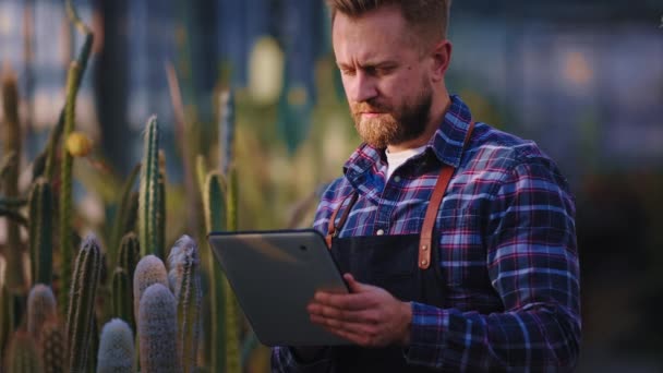 In agrarische kas goed uitziende man tuinier met een elektronische tablet maken enkele notities over de toestand van decoratieve planten. Neergeschoten op Arri Alexa Mini — Stockvideo