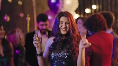 Beautiful and stylish lady in a sparkling dress enjoying the time at glamorous party dancing and smiling large while holding a glass of sparkling wine