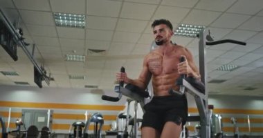 In front of the athletic man wish tattoo work hard in a modern gym he pumps up the legs doing exercises for his abs