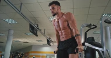 Büyük bir spor salonunda dövmeleri olan konsantre bir atletik adam sıkı çalışıyor. Bacaklarını kaldırıyor. Karın kasları için çalışıyor.