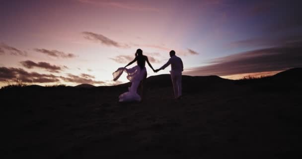 Tempo romântico ao pôr do sol para um jovem casal eles apreciam o tempo juntos caminhando pelo campo cheio de areia e pedras — Vídeo de Stock