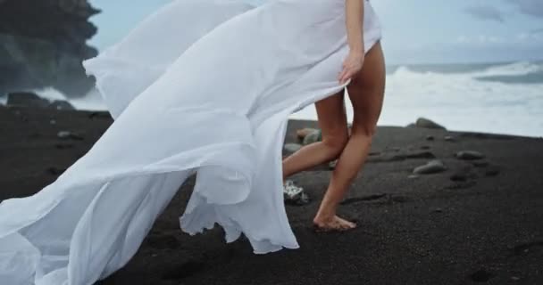 Vacker kvinna med perfekta långa ben i en vit klänning promenader genom stranden bredvid havet — Stockvideo