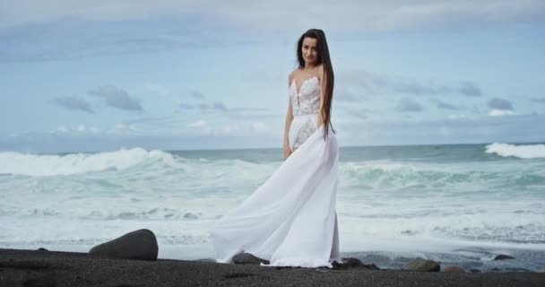 Hermosa mujer joven carismática caminando por el lado de la playa que llevaba vestido blanco increíble. 4k — Vídeo de stock