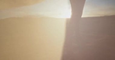 Güneşli bir günde, güzel bir elbiseyle kumsalda yürüyen uzun elbisesini tutan bir kadın.