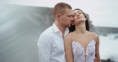 Harika manzaralı güzel bir sahil kenarında genç bir çift kameranın önünde romantik bir zaman geçiriyorlar birbirlerine sarılıyorlar ve birbirlerine bakıyorlar.