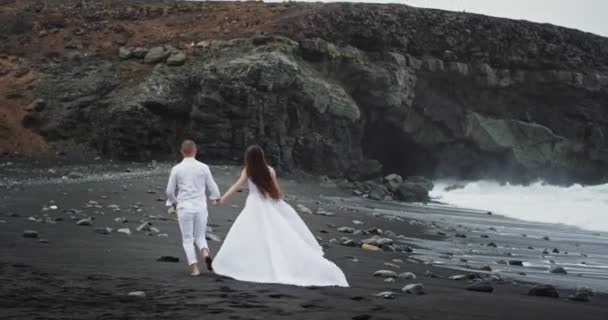 Al atardecer en medio de un hermoso paisaje con montaña y rocas pareja romántica corriendo mientras se toma de la mano — Vídeos de Stock