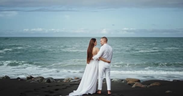 Hermosa playa con una arena negra de pie delante de la playa increíble pareja en el amor que tienen un momento romántico besándose con pasión — Vídeos de Stock