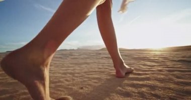 İnanılmaz bir manzaranın ortasında genç bir kadın elinde uzun ve beyaz elbisesiyle kum ve taşlarla tarlada yürüyor.